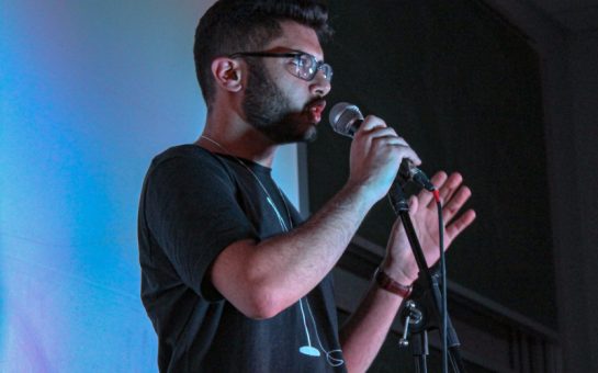 Rohan Ashar speaking into a microphone, performing at comedy show