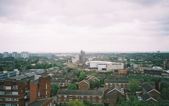 Image taken from Caledonian Park Clocktower, in Islington. Views over market estate housing estate and city suburb skyline further on, with some green space, and grey sky visible at the top.