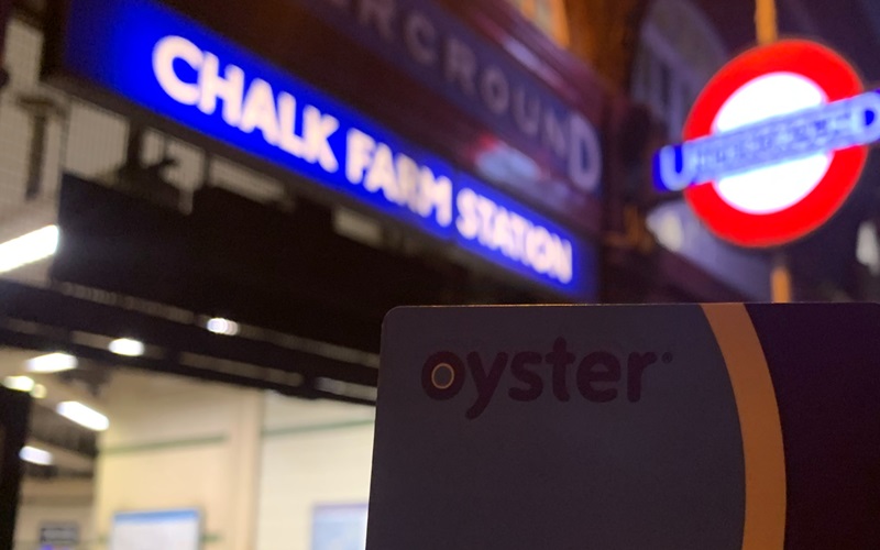 A close-up of an Oyster card, the travel card for London's public transport system. The background is Chalk Farm Underground Station.