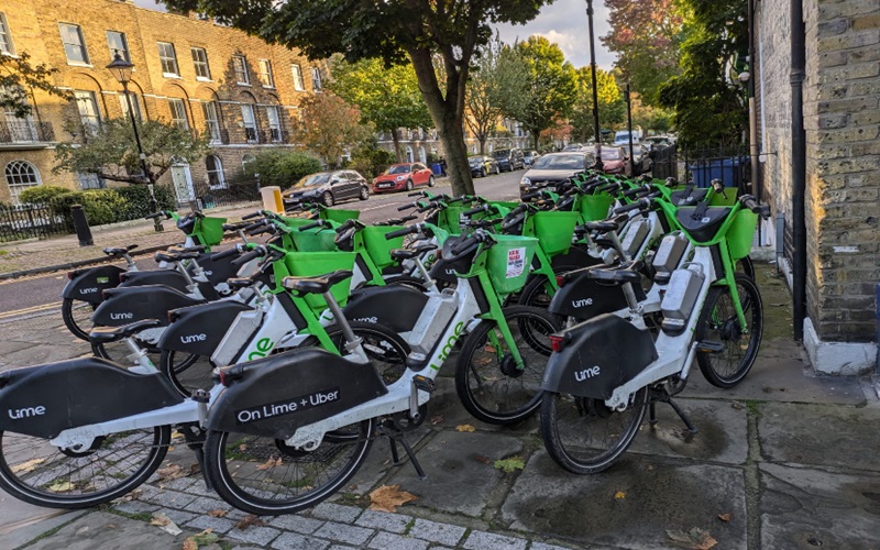 A cluster of Lime e-bikes and Uber-branded bikes are parked haphazardly on a sidewalk, blocking pedestrian access.