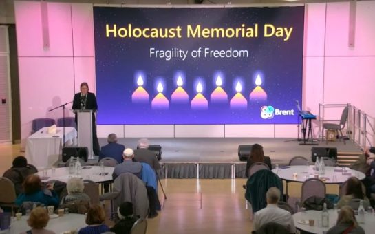 Image of people attending a talk with a screen behind with the title 'Holocaust Memorial Day'