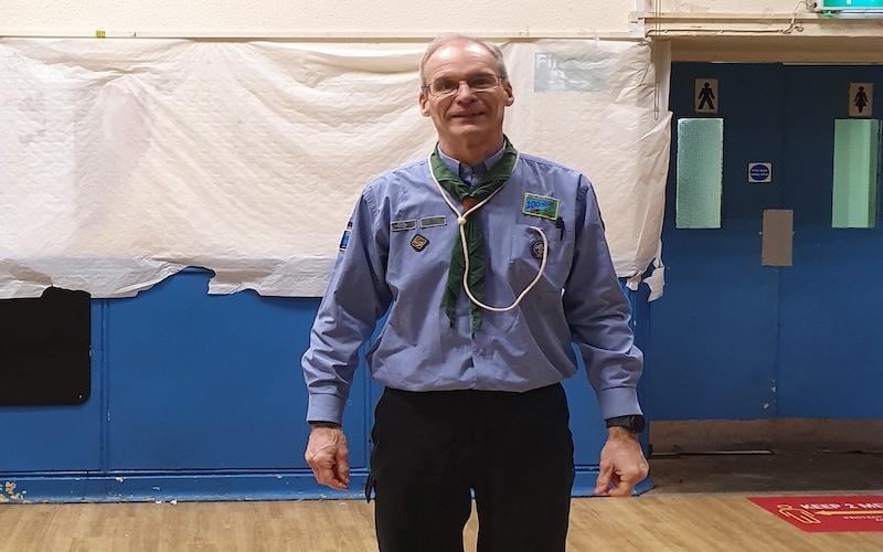 Scout leader Mark Thompson stands in his community hall in his uniform.