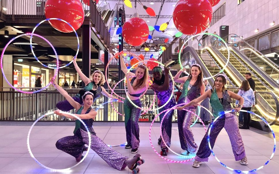 Dancers with hula hoops and roller skates posing with lights and balloons behind.